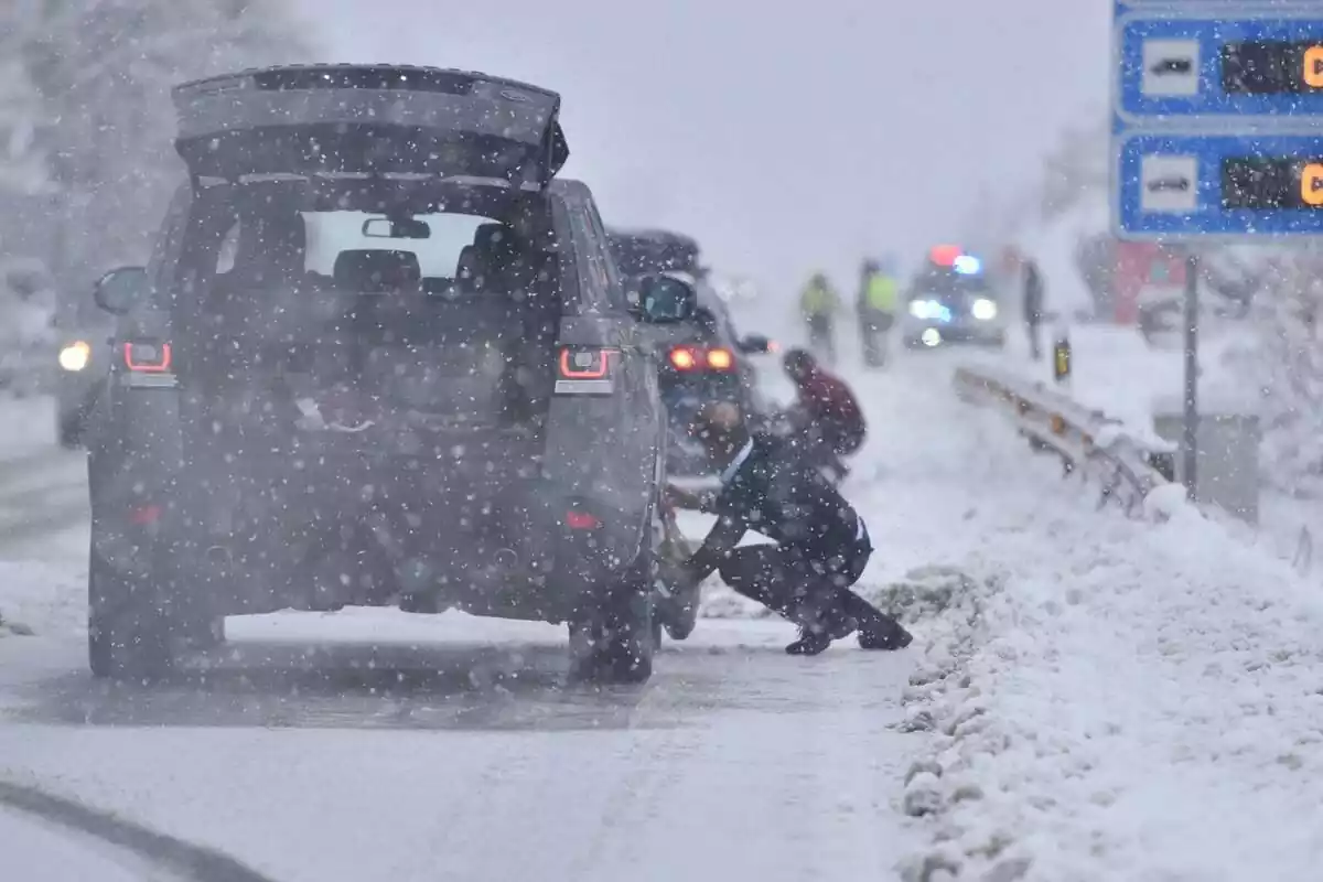 Varios conductores colocando cadenas en las ruedas en medio de una intensa nevada