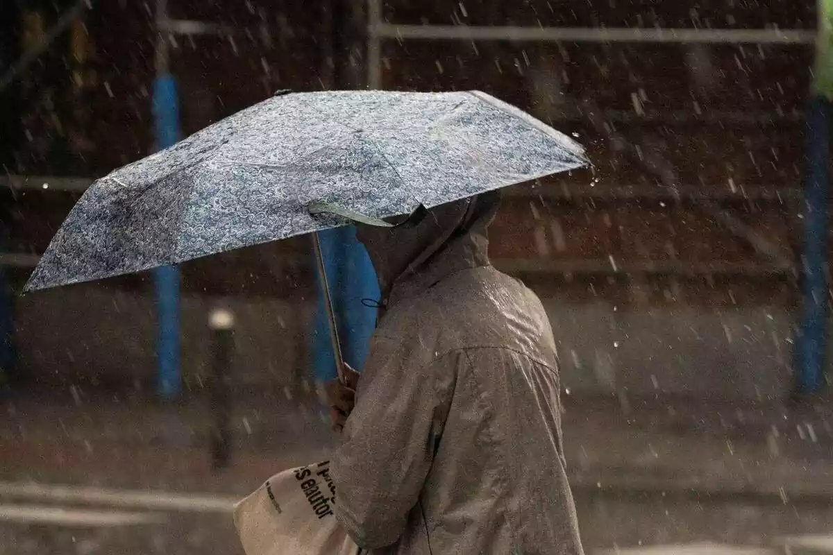 Imagen de una persona con un paraguas en la mano debajo de la lluvia.