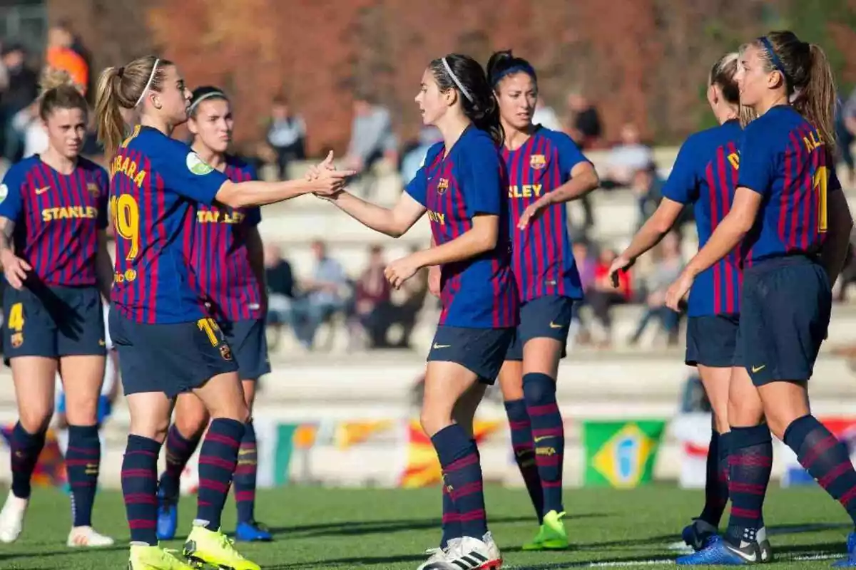 Imagen de las jugadoras del Barça Femenino en un campo de fútbol. Dos jugadoras se están dando la mano