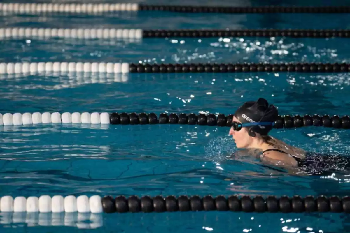 Una mujer nadando en una piscina con carriles divididos por bolas negras y blancas