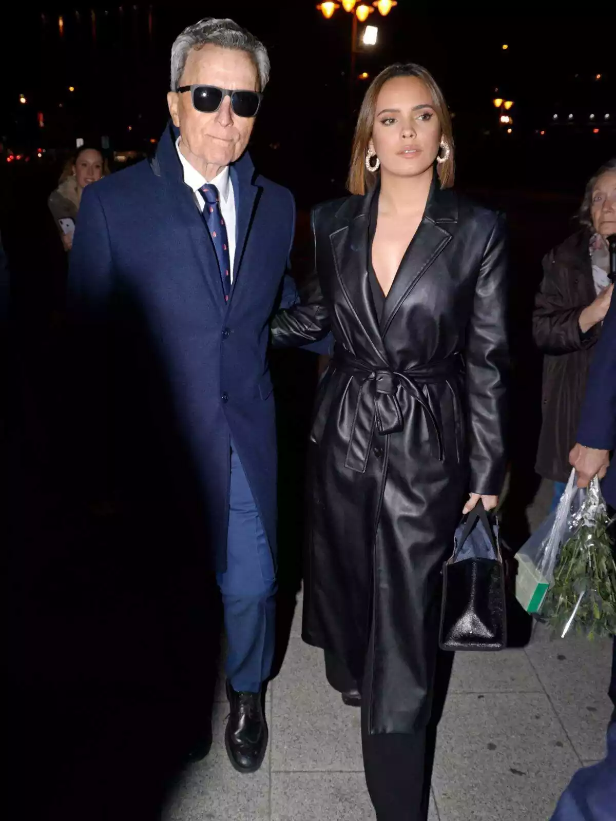 José Ortega Cano con gafas de sol y corbata azul, y Gloria Camila Ortega seria con una gabardina negra