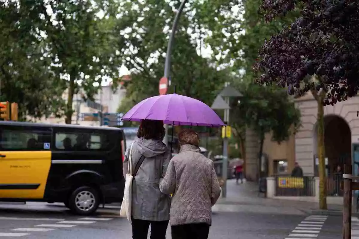 Imagen de dos personas paseando bajo la lluvia en Barcelona
